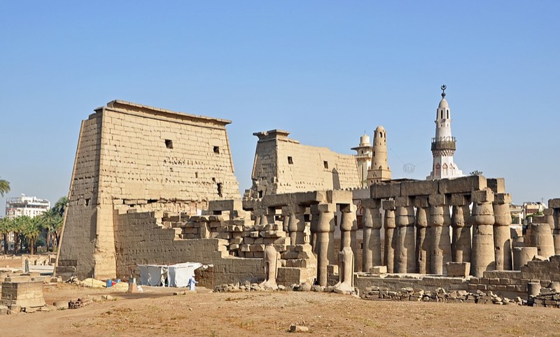 Pylons and obelisk of Luxor Temple at twilight with lights illuminating the sandstone columns
