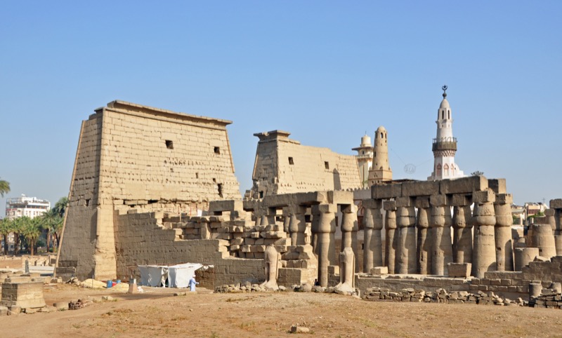 The illuminated pylons and obelisk of Luxor Temple at dusk, with the Nile visible in the background